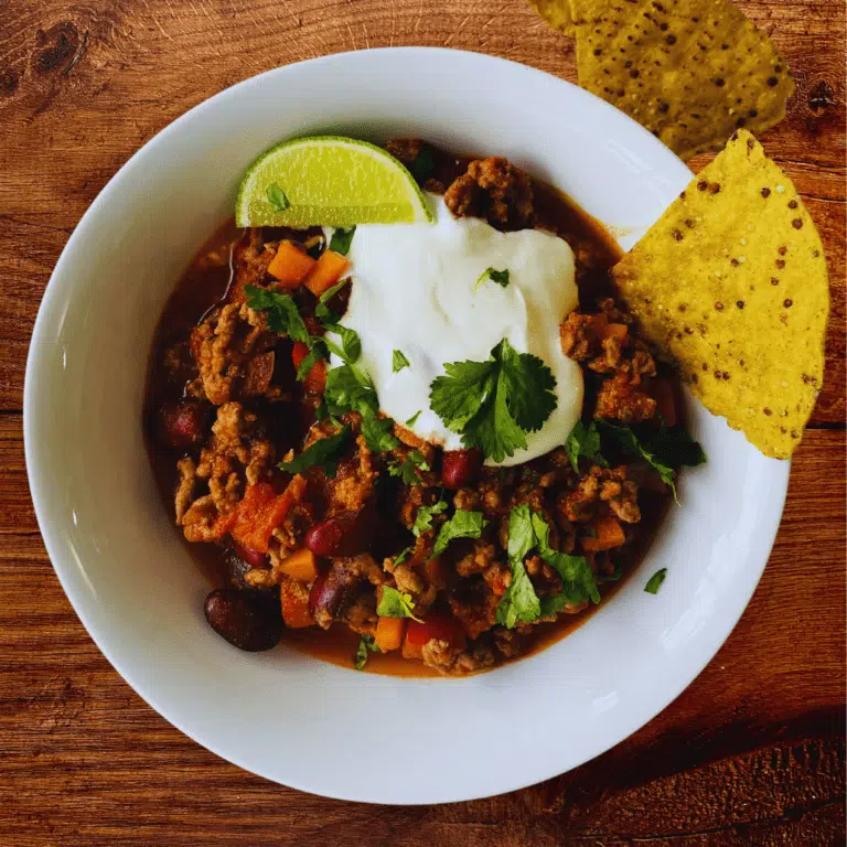 a bowl of chilli con carne with a slice of fresh lime, tortilla chips, yogurt and cilantro